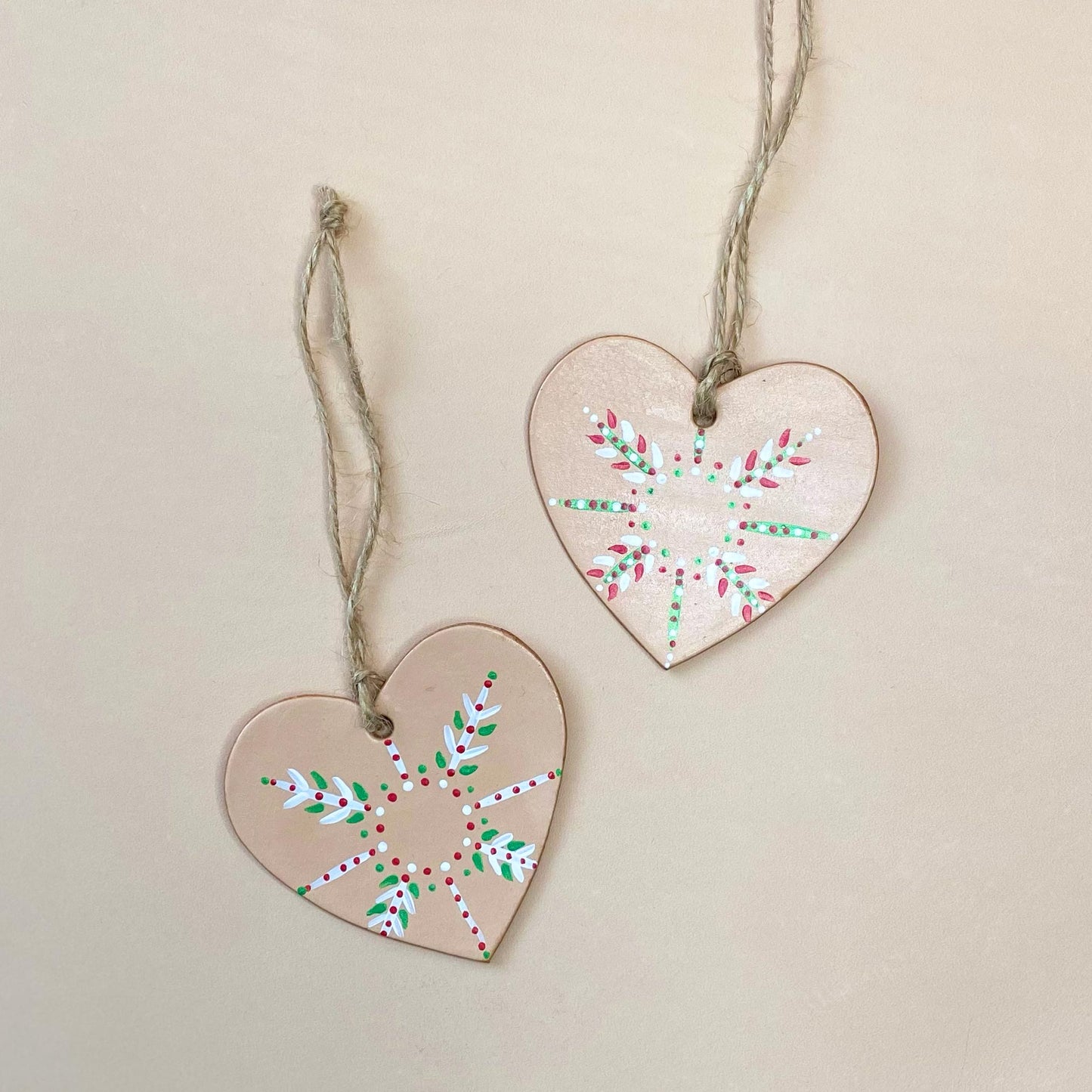 Two heart shaped Christmas ornaments painted with colourful snowflake designs sit on a neutral background