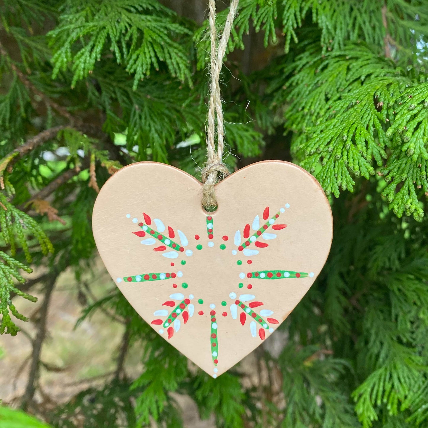 A heart shaped decoration painted with a colourful snowflake design hangs in a Christmas tree