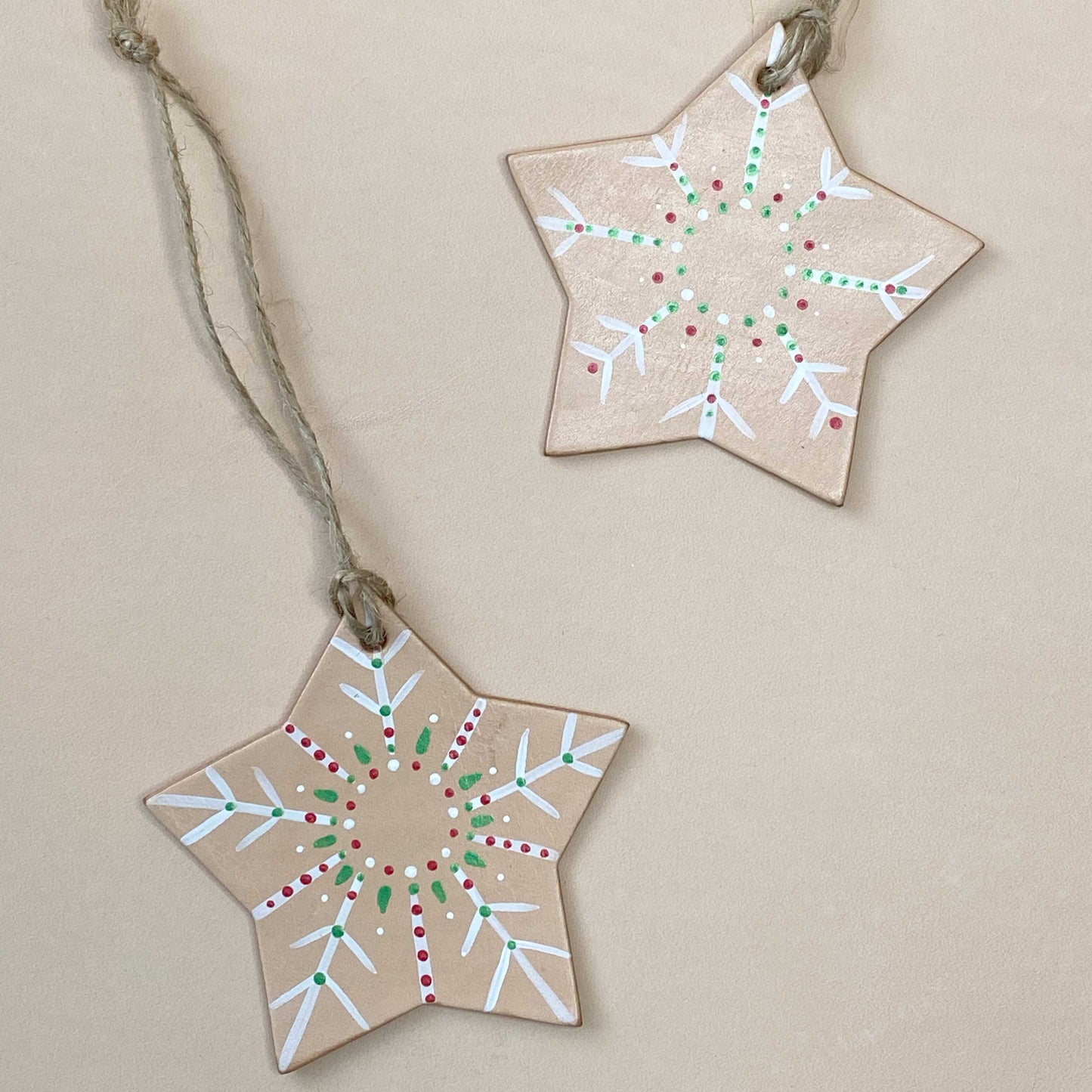 Two star-shaped leather decorations with painted patterns on a beige background