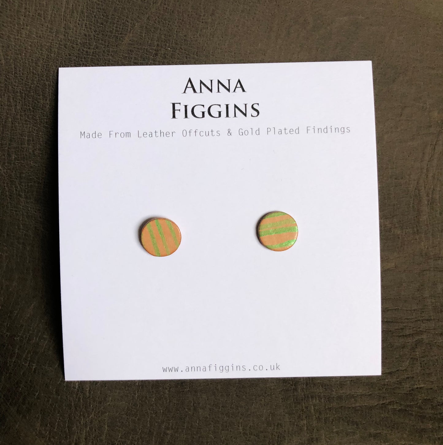 A pair of green striped leather stud earrings on their display card