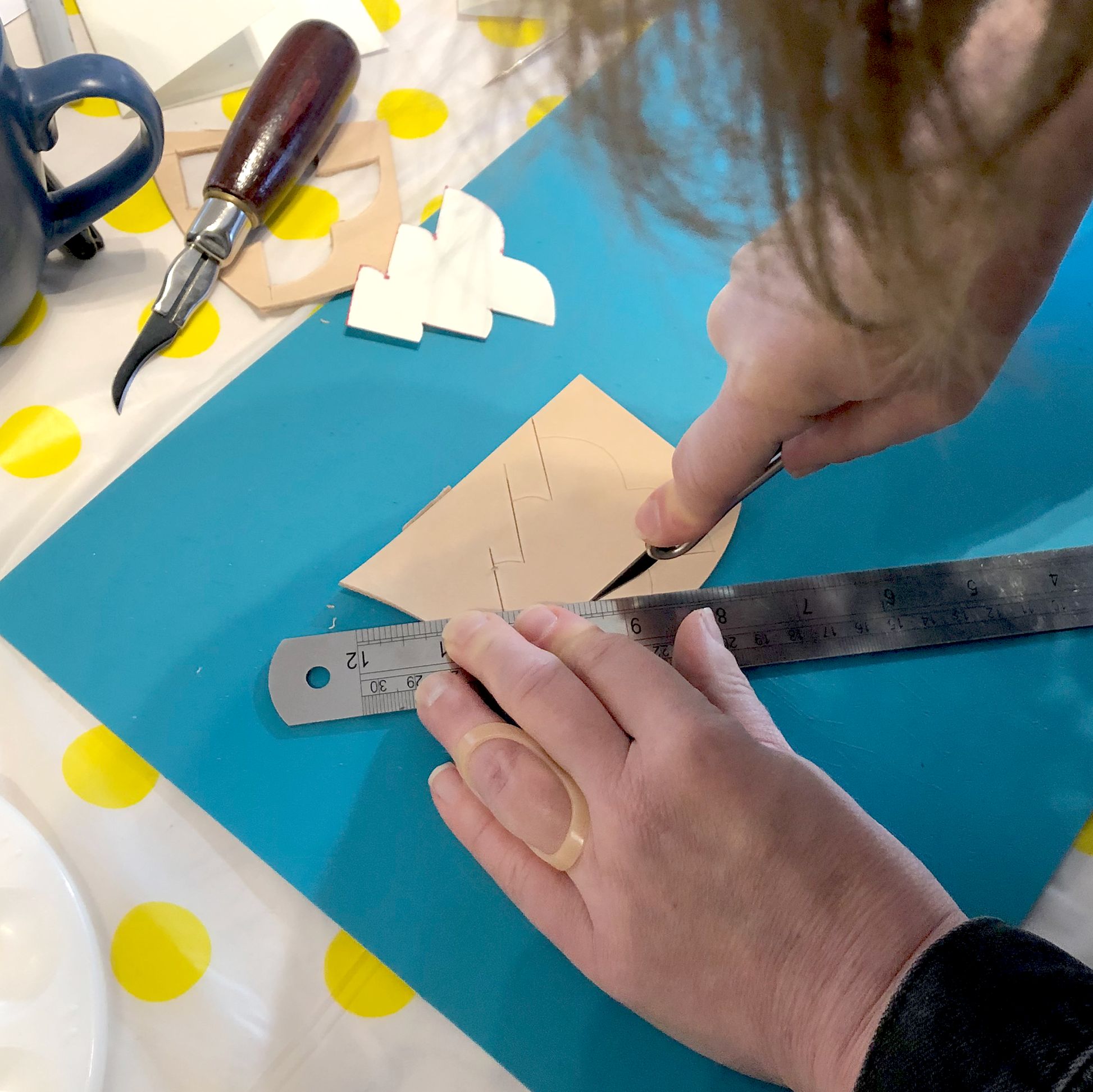 A PAIR OF HANDS IS USING A SCALPEL AND A METAL RULER TO CUT A PIECE OF LEATHER INTO A CHRISTMAS TREE SHAPE