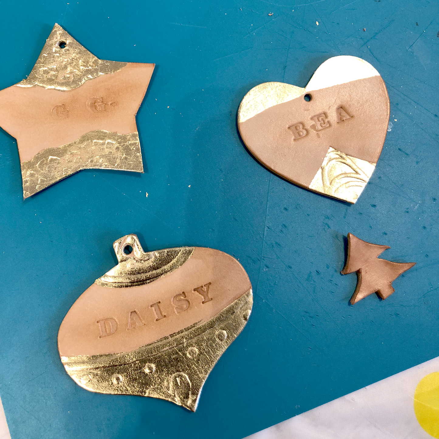 3 FINISHED LEATHER CHRISTMAS DECORATIONS. ONE IS SHAPED AS A STAR, ANOTHER A HEART AND THE LAST ONE A VINTAGE BAUBLE. EACH HAS BEEN EMBOSSED, STAMPED WITH A NAME OR INITIALS, AND DECORATED WITH GOLD COLOURED METAL LEAF