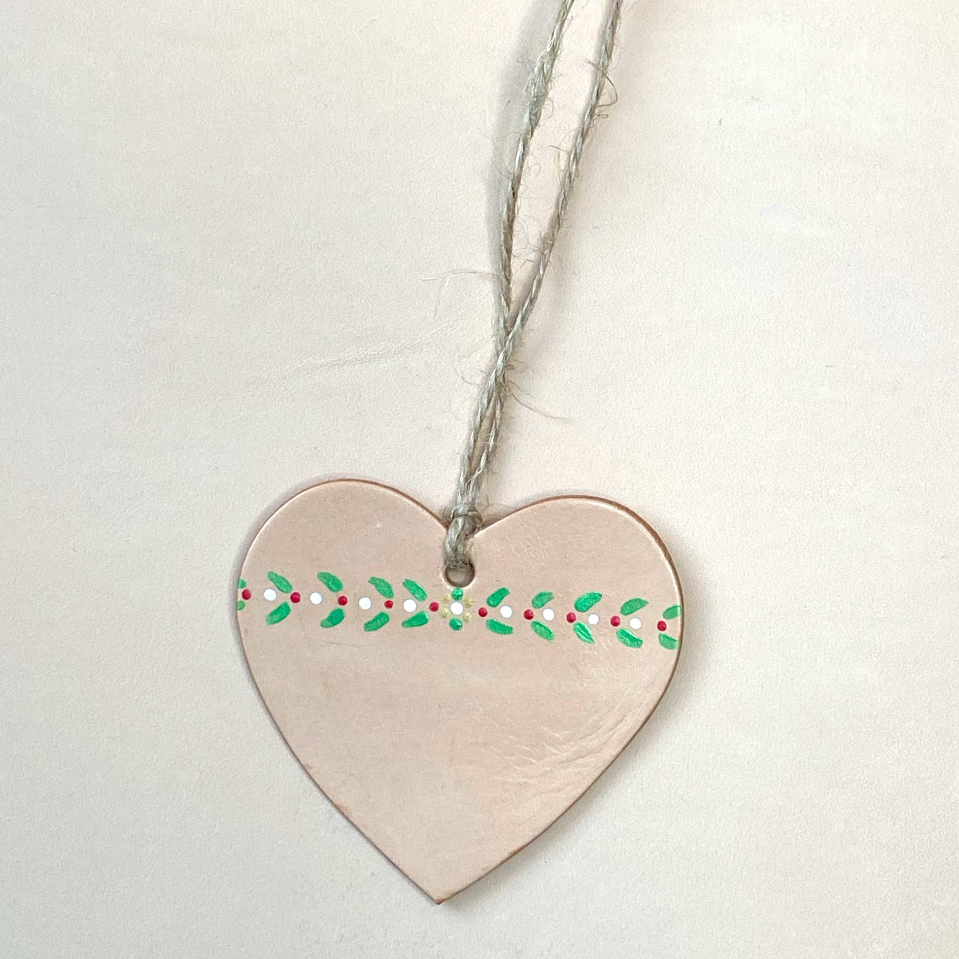 A hand-painted heart shaped Christmas ornament on a neutral background