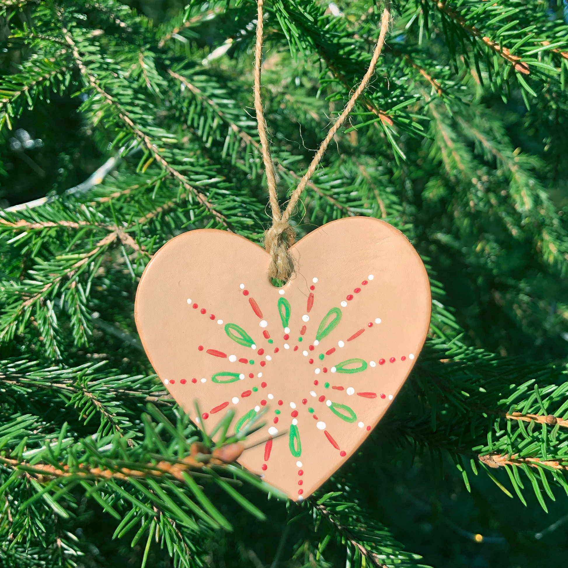 A leather heart decoration painted in a red, green and white festive pattern is hanging in a Christmas tree. 