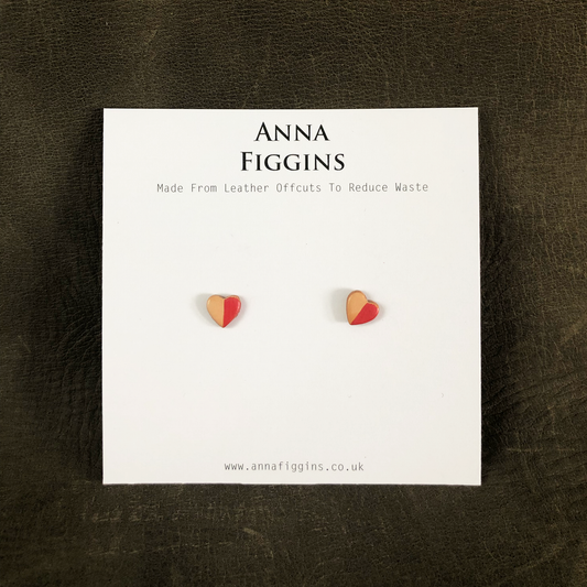 A pair of small heart shaped leather stud earrings on their display card. Half of the hearts have been painted with red pearlescent paint