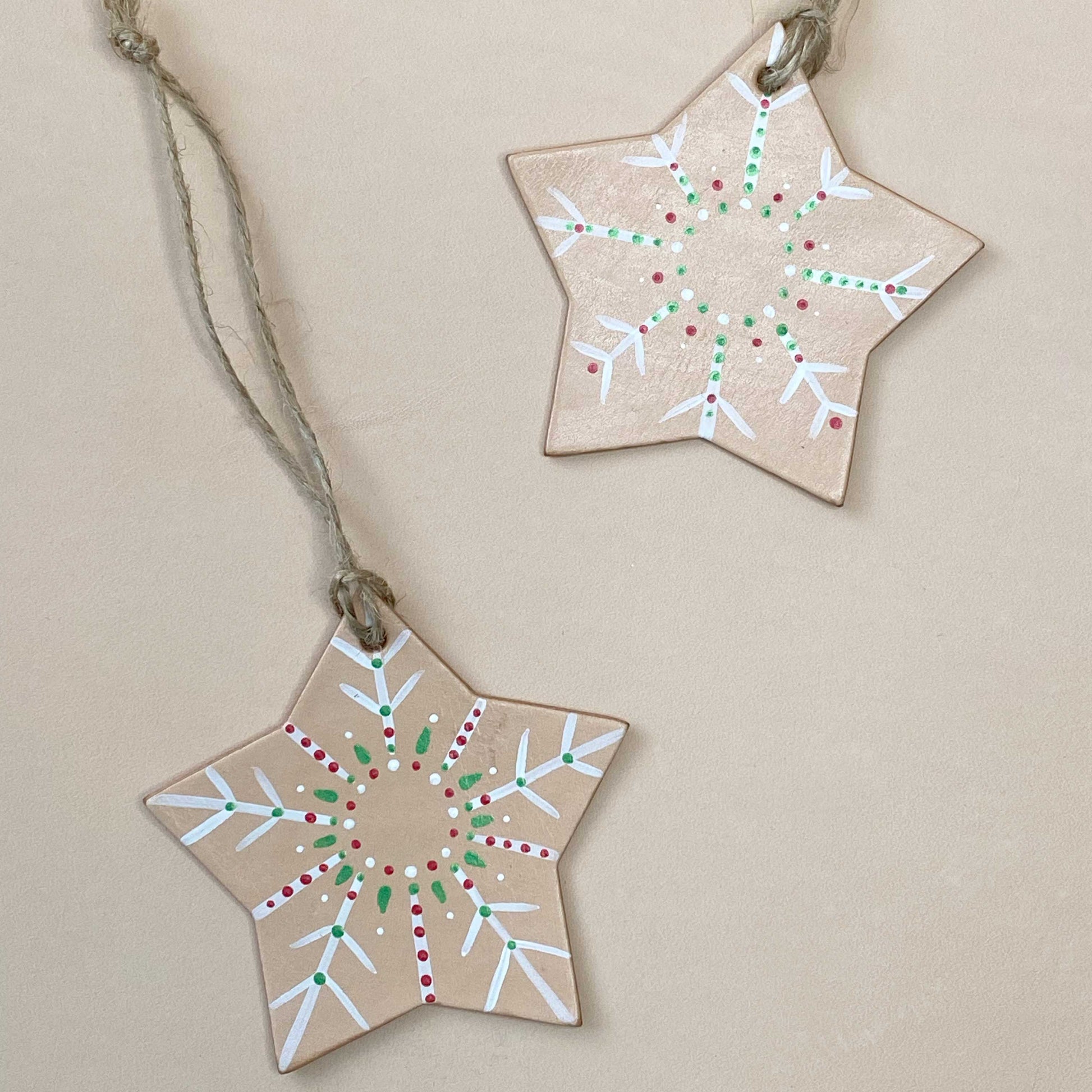Two star-shaped leather decorations with painted patterns on a beige background