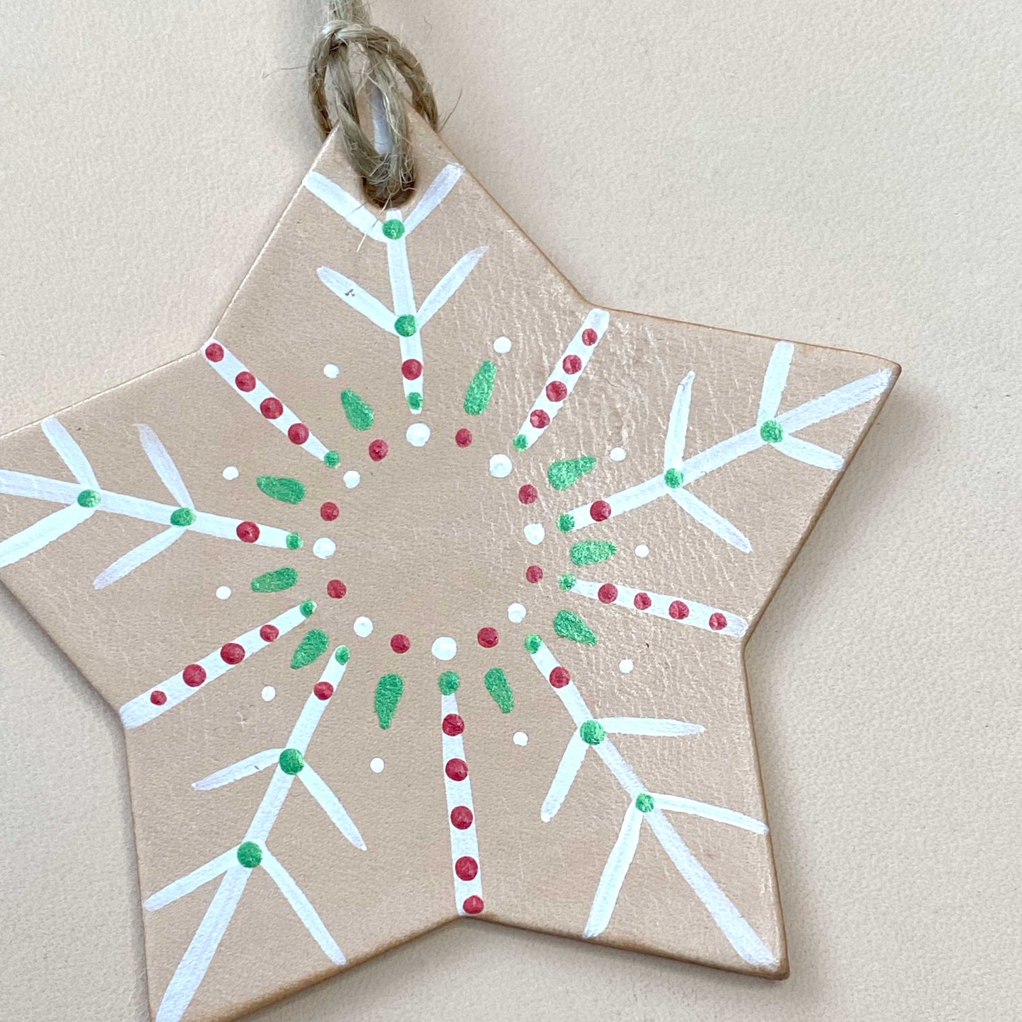 Star-shaped decorative tree ornament with white, red, and green patterns on a beige background
