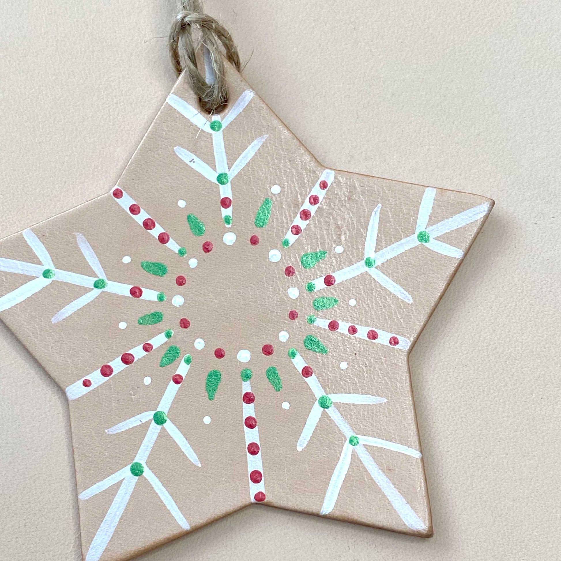 Star-shaped decorative tree ornament with white, red, and green patterns on a beige background