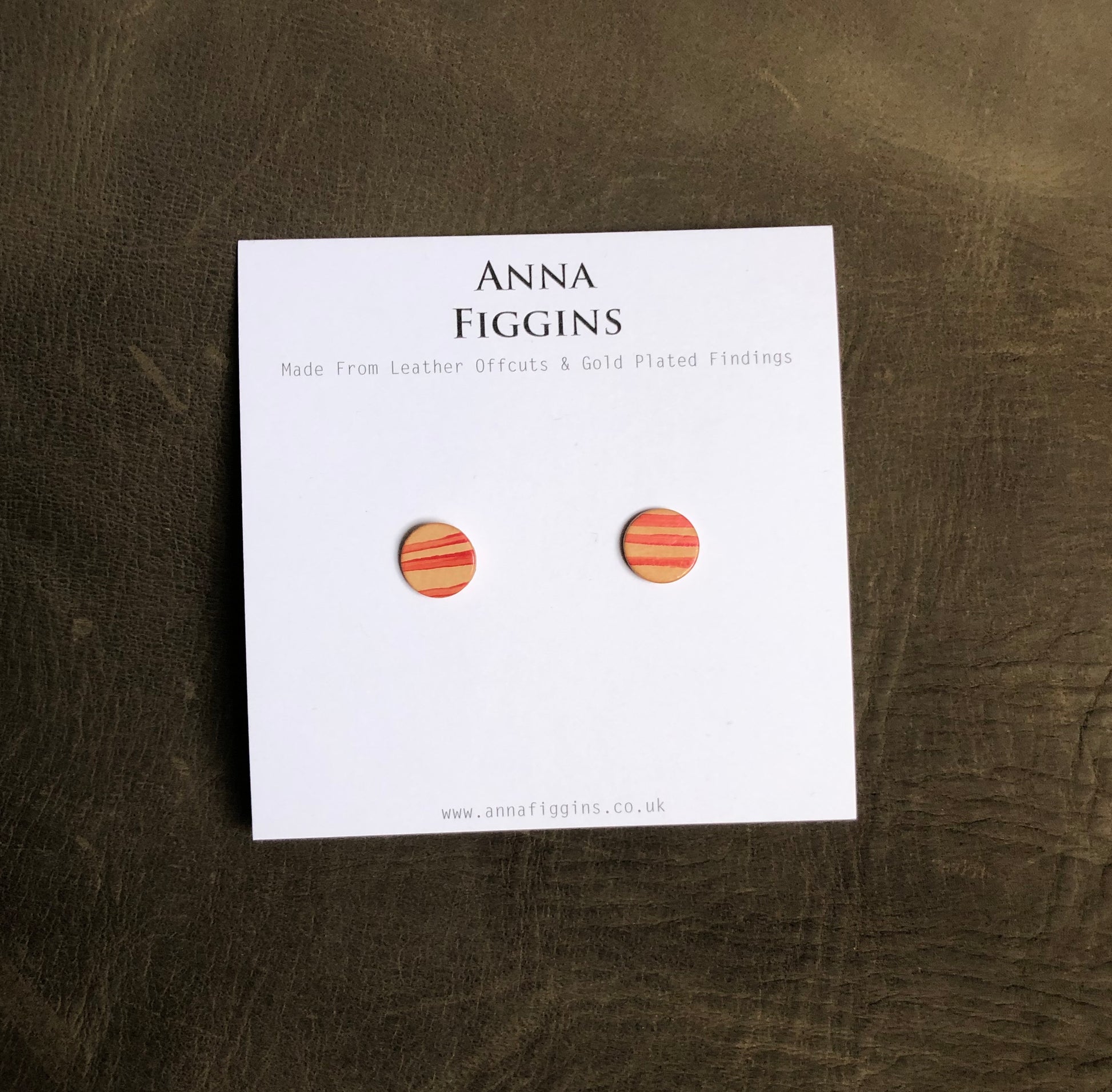 A pair of red striped leather stud earrings on their display card
