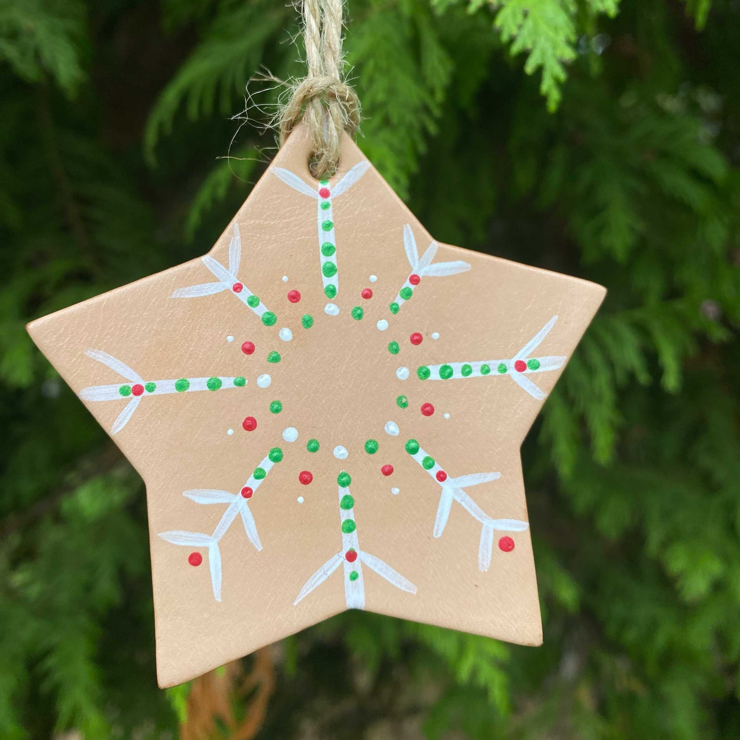 Star-shaped leather Christmas ornament with a dotty snowflake pattern hanging against a green tree background.