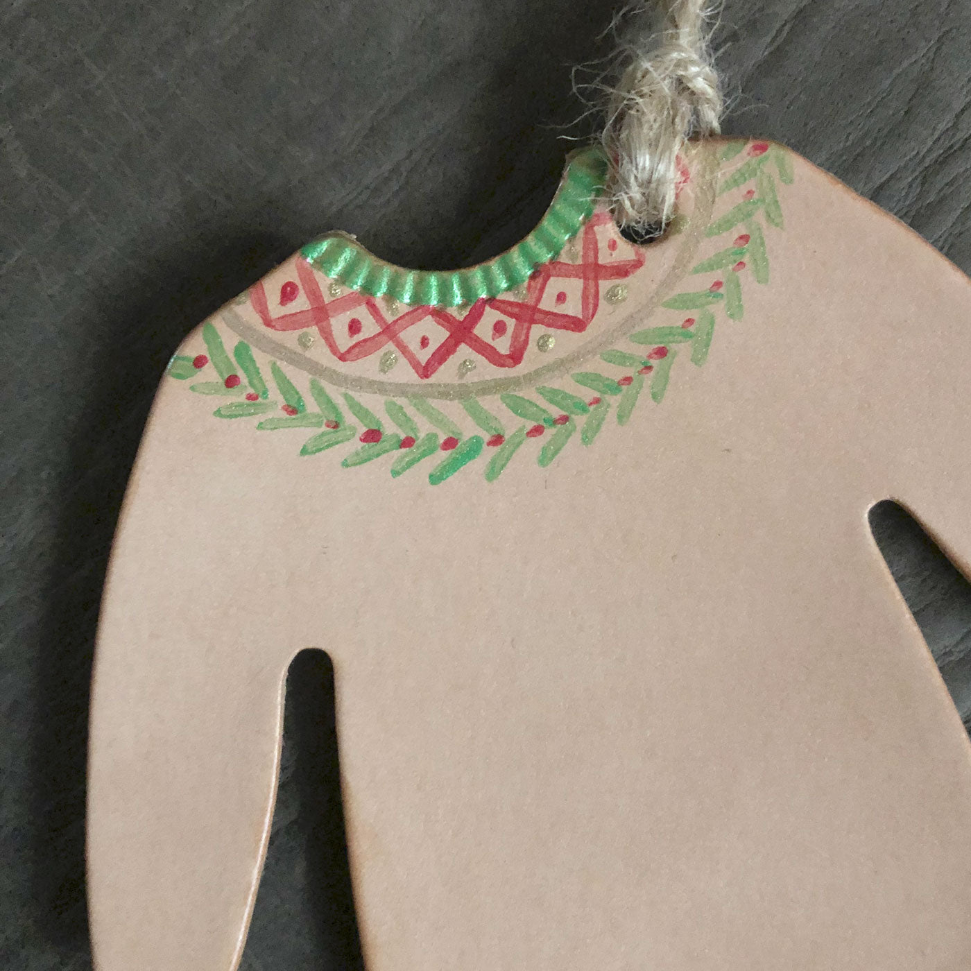 A close up of part of a hand painted leather Christmas jumper tree decoration. It is a lose up shot of the neck area, which has been painted in a festive design in green, gold and red