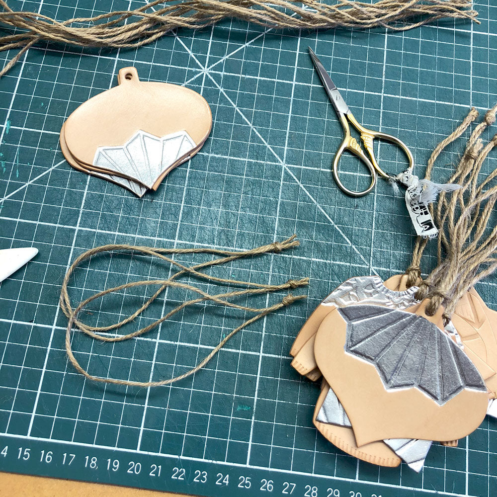 A SELECTION OF LEATHER CHRISTMAS DECORATIONS. SOME ARE COMPLETE AND OTHERS WAITING TO BE STRUNG. THEY HAVE BEEN EMBOSSED AND DECORATED WITH SILVER COLOURED METAL LEAF